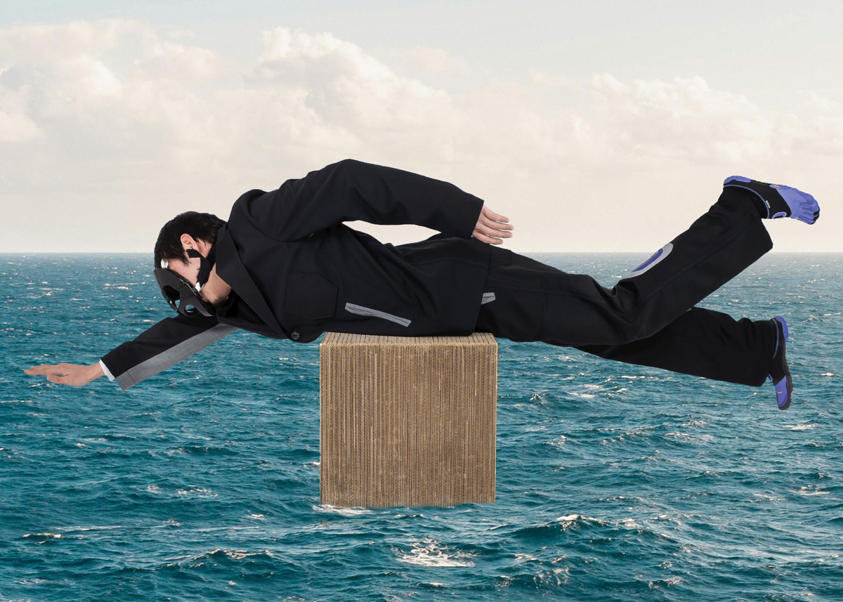 A man in a black suit with a black hockey mask and blue webbed footwear lays on a wood block over a photoshopped image of the ocean.