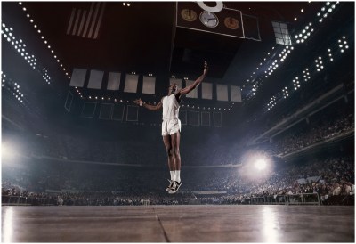 A photograph showing a Black basketball player soaring in the air on a court.