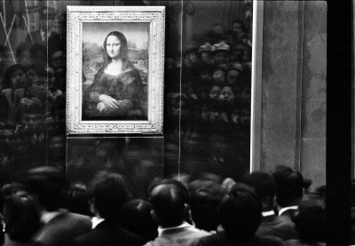 Painting of a smiling woman behind glass with a crowd before the painting.