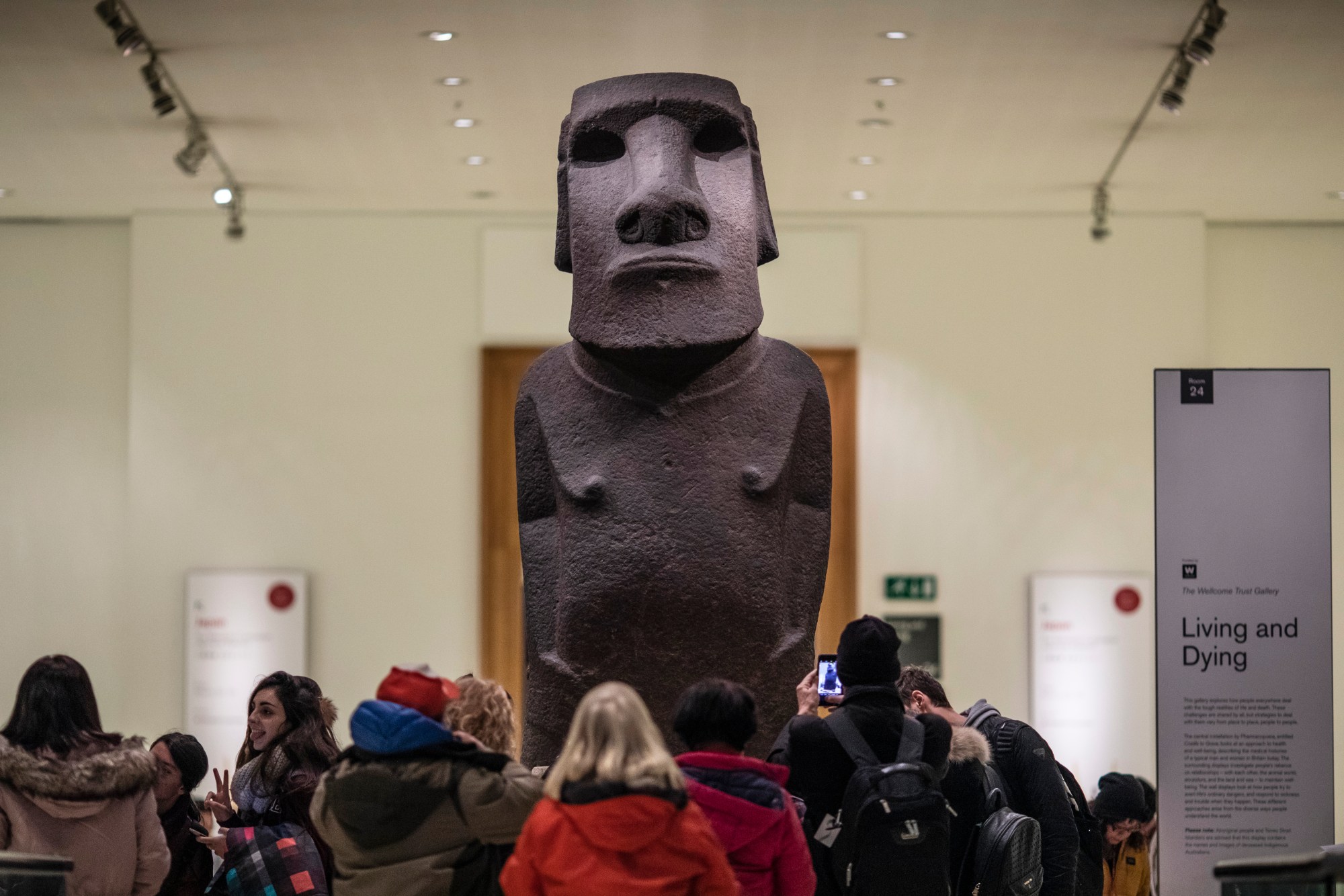 A large basalt sculpture of a shirtless figure with a large face. The sculpture towers above people who stand below.