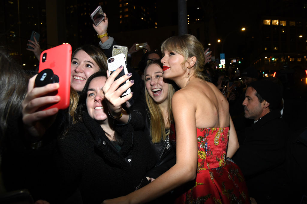 A white woman posing for a selfie beside smiling fans.