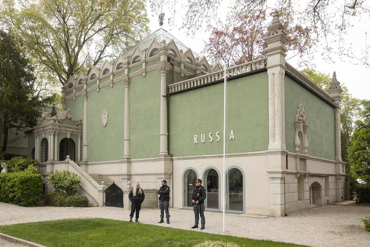 Three guards standing before a blocky green pavilion that has the word 'RUSSIA' on its columned facade.