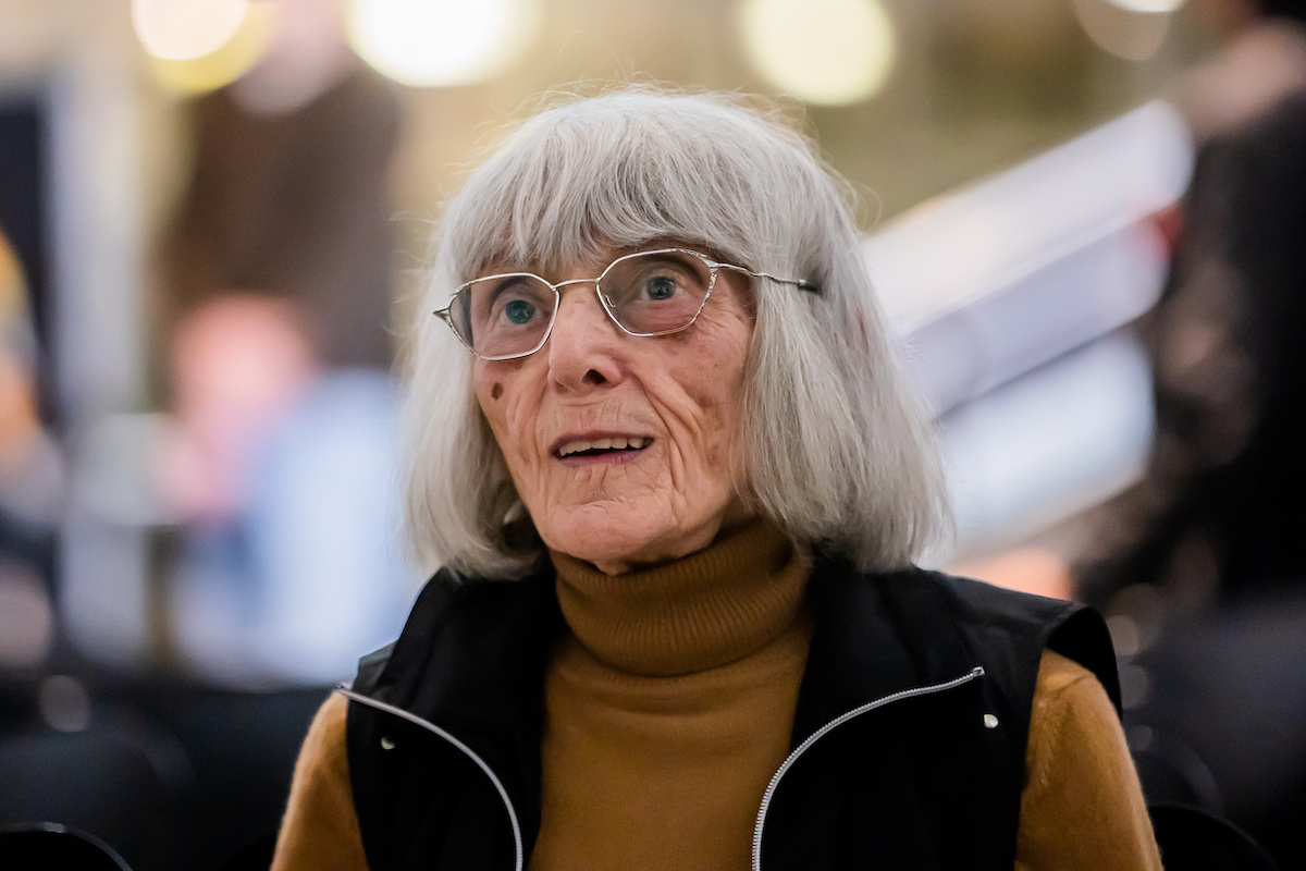 An elderly white woman with glasses and short-cropped white hair in a black vest.