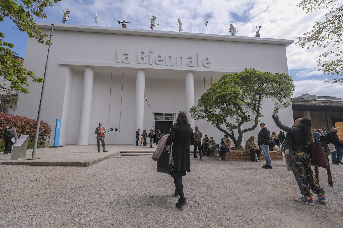 Crowds of people in front of a white columned building with 'la Biennale' on its facade.