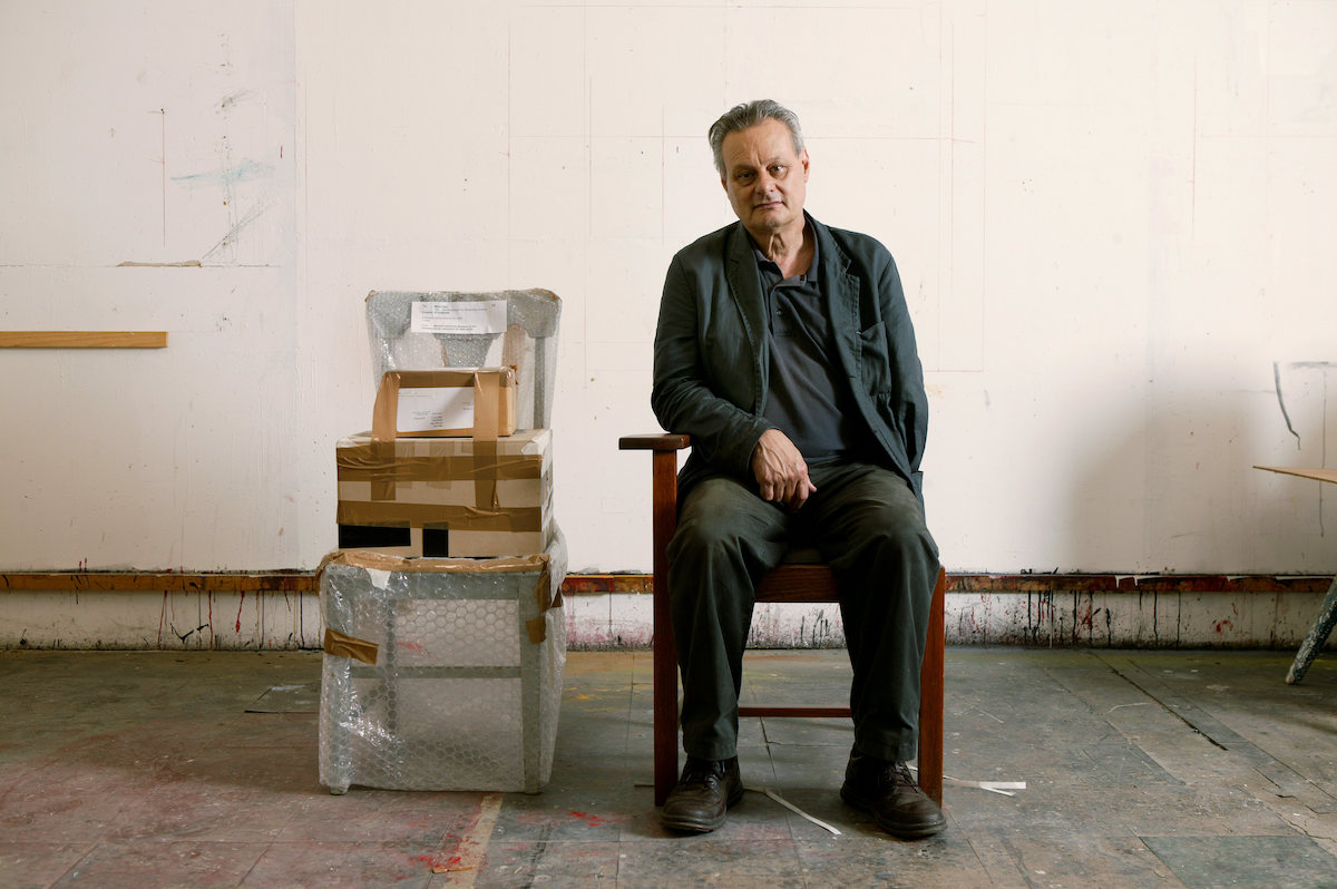 A mean seated in a chair beside another chair in bubble wrap with a box on it.