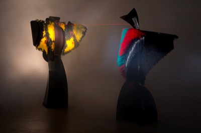 Two abstract sculptures, with a laser pointing from one red and blue one onto another whose yellow parts resemble wings.