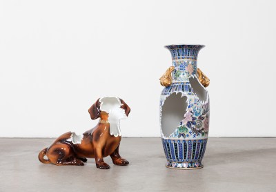 A porcelain sculpture of a Dachsund and porcelain vase that are smashed in parts.