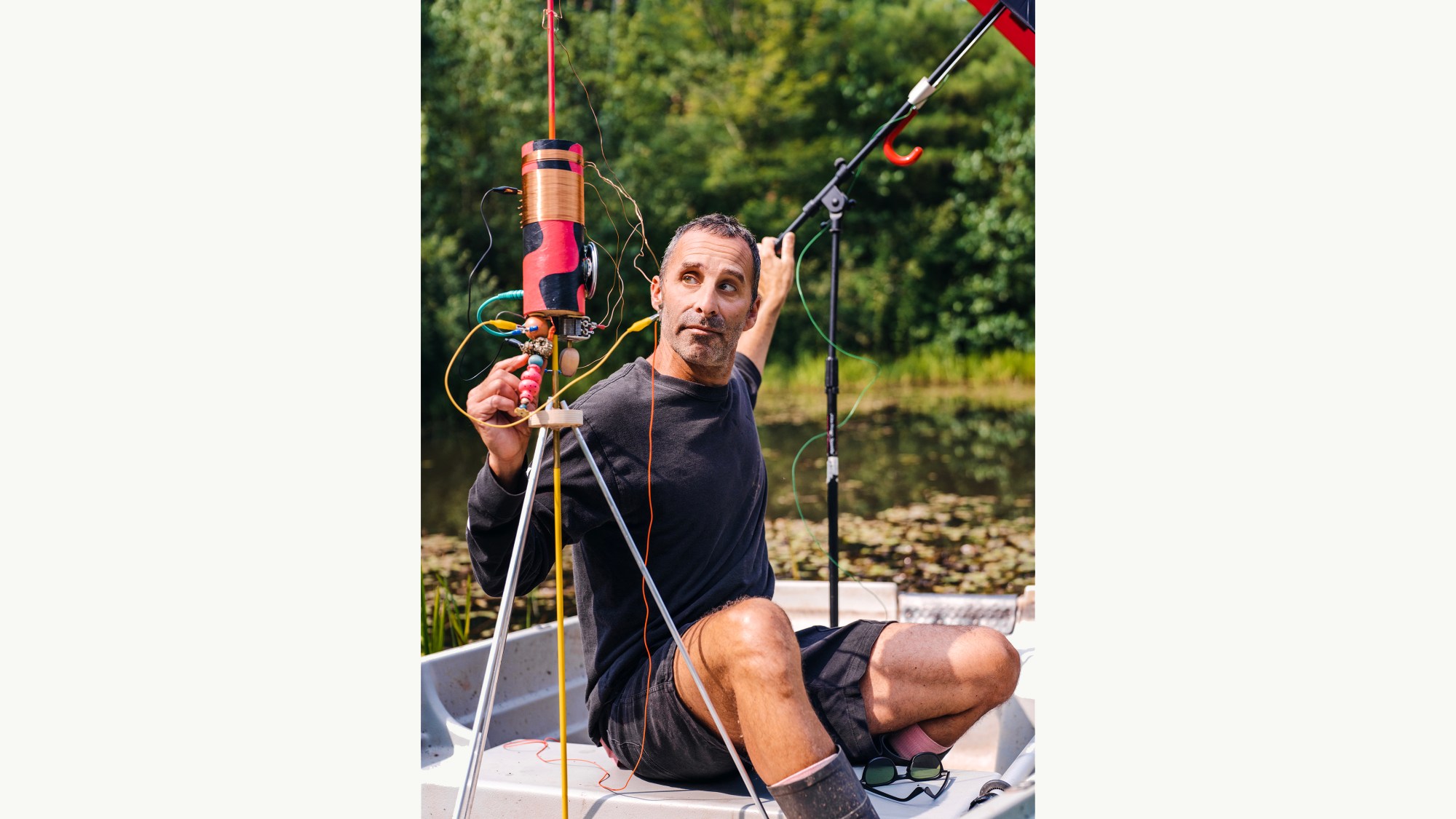 A White man sits on a boat while working with different types of equipment