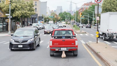 a red ford pickup truck modified so the body of the vehicle is backwards driving down a road next to unmodified vehicles.