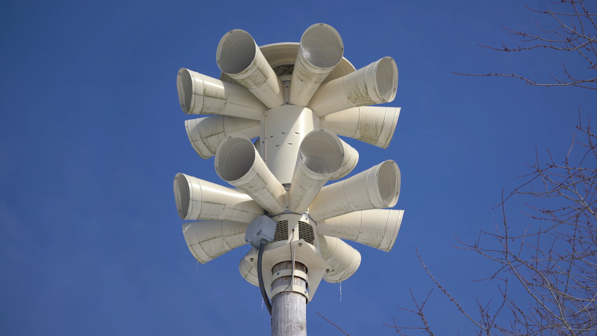 A dozen or so white sirens atop a metal pole against a deep blue sky.